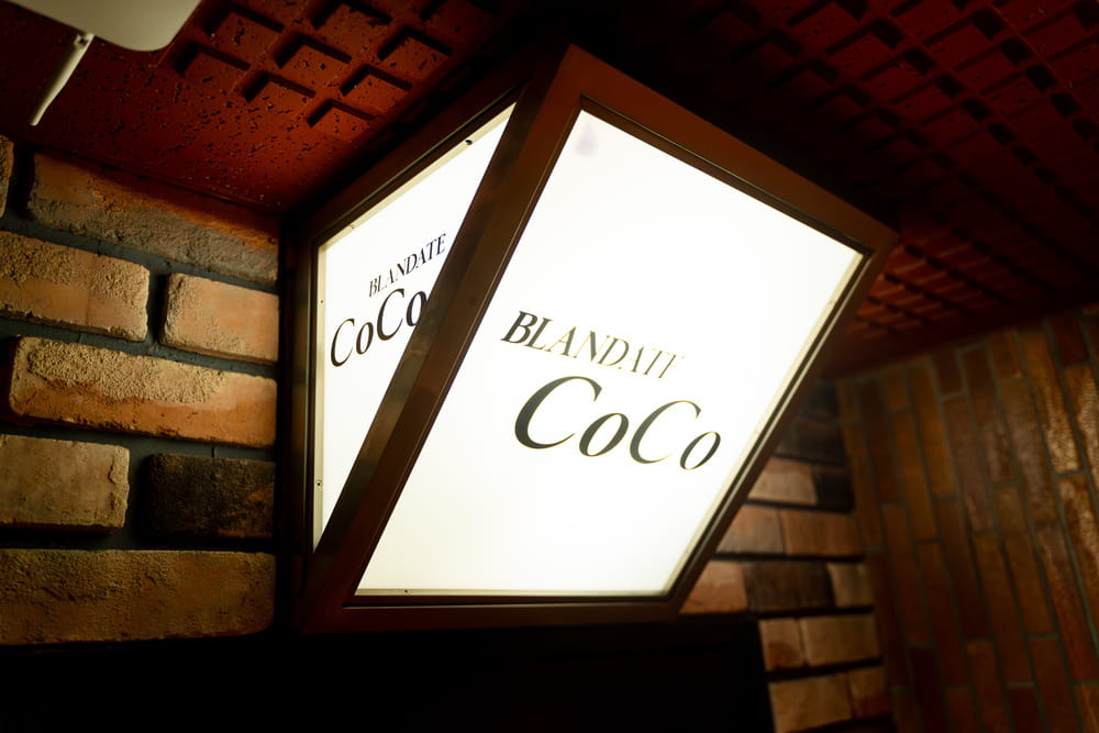 レンガ壁に取り付けられた「BLANDATE CoCo」のロゴ入り看板　落ち着いた雰囲気の外観